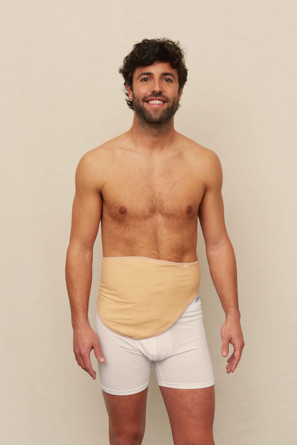 Shirtless man in white boxer briefs with a beige ostomy belt around his stoma