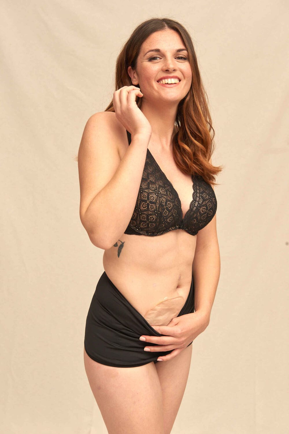 Brunette in a black lace bra holding her pouch under a black Basic ostomy wrap