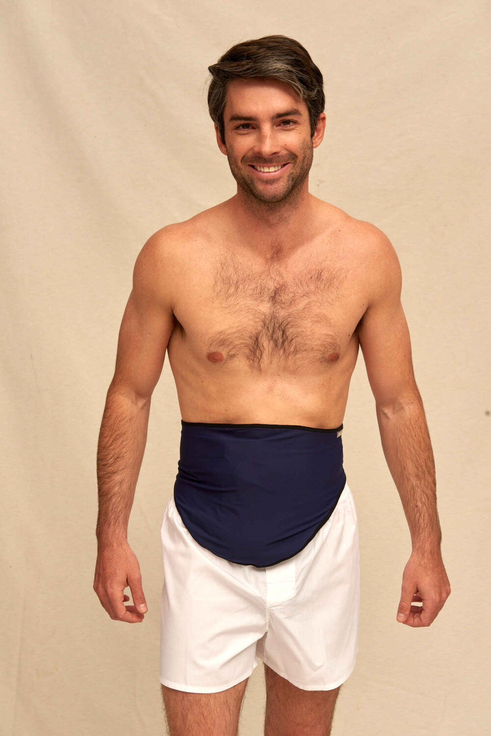 Shirtless man in white boxer shorts wearing a navy ostomy support belt as his bag cover