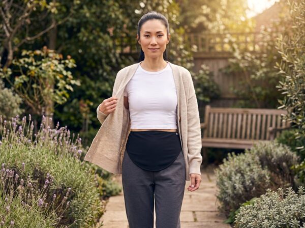 Colostomy surgery recovery: woman in a soft cardigan smiling on a slow walk down her garden path, black SIIL stoma belt at her waist