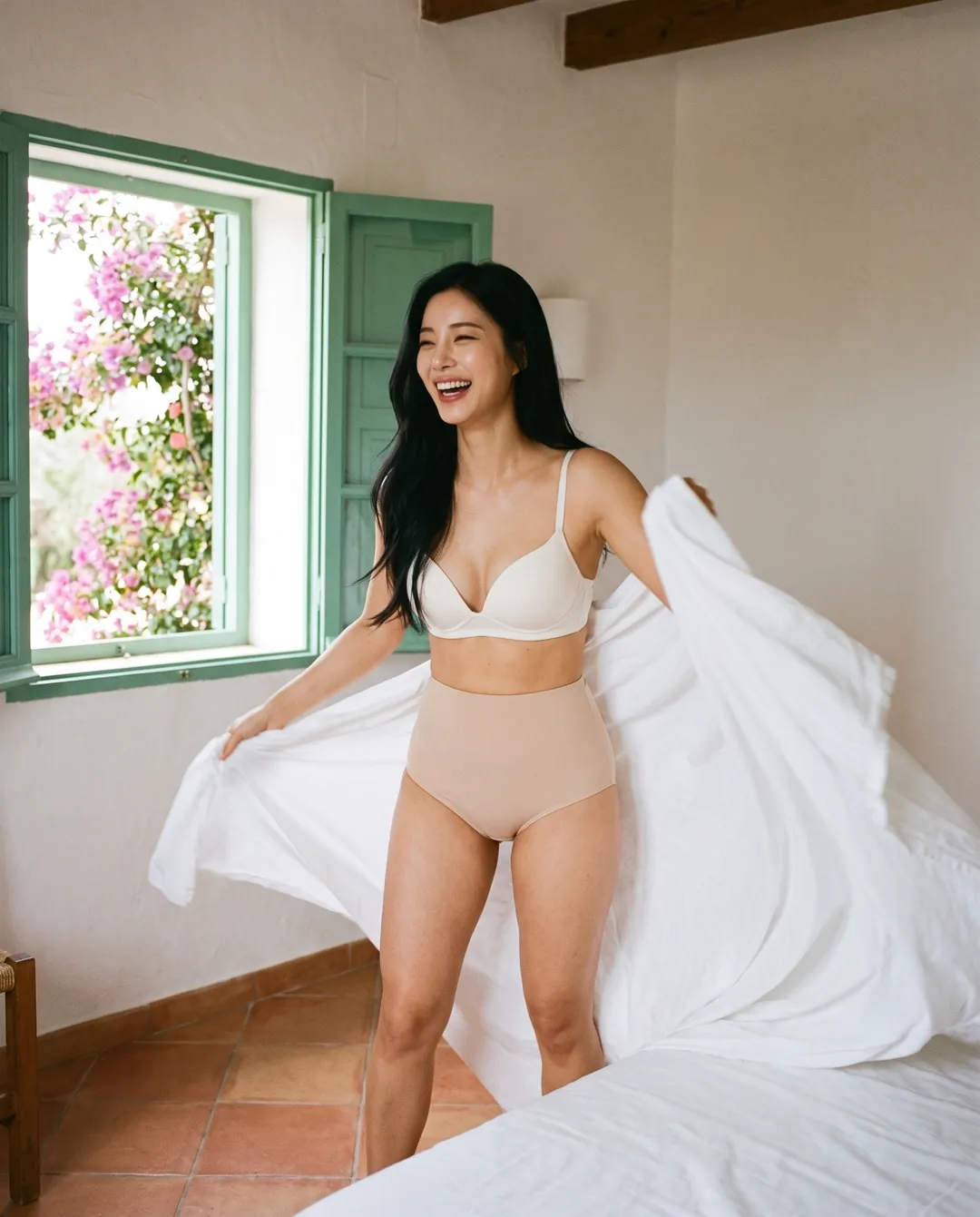 Woman laughing as she shakes out a fresh white sheet, wearing beige SIIL Classic ostomy panties